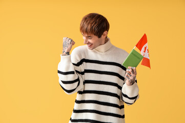 Canvas Print - Handsome young man with flag of Canada and passport celebrating success on yellow background. Immigration concept