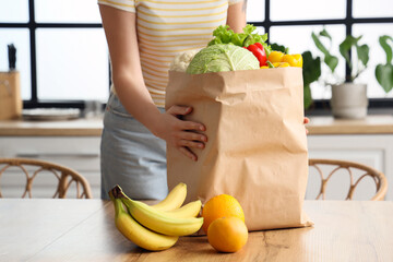 Wall Mural - Young woman with paper bag of healthy food in kitchen, closeup