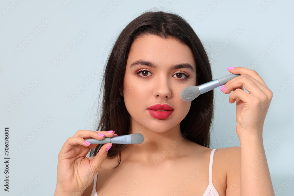 Beautiful young woman with makeup brushes on blue background