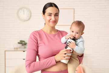 Poster - Beautiful young sporty woman with bottle of water holding her little baby at home