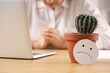 Cactus and sad smile on table of mature businesswoman with hemorrhoids in office, closeup