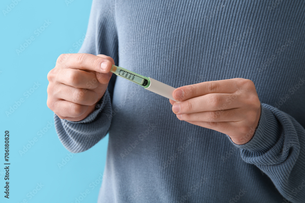 Diabetic young man using lancet pen on blue background