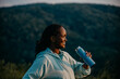 Black woman enjoying a jog, pausing to sip refreshing water