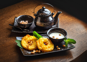 Sticker - Asian sweets and tea. Fried pineapple slices in batter, coconut milk sauce, ceramic teapot and a bowl with cane sugar.