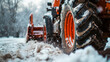 Red tractor with a snow plow attachment working on snow removal on a road, showcasing the concept of winter road maintenance, close-up.