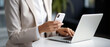 © bagotaj - Business woman in grey suit using mobile phone while working on a laptop computer.