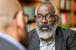 Close-up image of a serious elderly African American man with glasses listening intently during a conversation indoors.