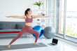 © Nopphon - Beautiful smiling Female wearing sportswear exercise training yoga in living room. Attractive asian young fitness woman stretching body warming up before workout at home.