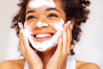 Close up of young beautiful darkskinned woman cleaning her skin with facial wash.