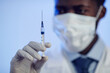 Close up shot with selective focus on syringe with vaccine in gloved hand of Black male doctor wearing face mask