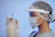 Side view of female nurse wearing protective medical face shield and mask while removing air bubbles from syringe with vaccine
