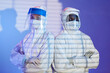 Medium shot of diverse man and woman laboratory technicians in white hazmat suits and face shields standing shoulder to shoulder while looking at camera