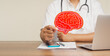 Brain health and dementia. Doctor holds a red brain symbol while sitting at a desk in the hospital.