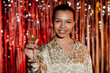 Medium close up shot of smiling African American girl at party looking at camera while holding glass of champagne in defocused foreground