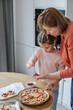 © Hanna - Caucasian woman 60 years old with a girl 8 years old spread jam on cookies in a bright kitchen