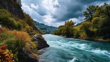 A Rushing River Through A Green Landscape Under Precise Clouds Creates A Dynamic And Picturesque View.