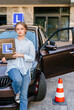 © Iryna - Vertical shot of girl poses near learner's car with an L sign on the roof. She holds a traffic cone and a folder with the letter L in her hand. Concept of learning driving skills in driving school.