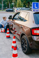 Vertical shot of disappointed girl student driving school sitting near a traffic cone after a failed parking attempt. Precise driving required: License test includes car handling around traffic cones.