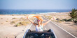 © simona - Happy women traveler enjoy road trip with a convertible car. One woman outside the roof have fun. Scenic desert destination. Car driving. Excited couple of friends in a vehicle on travel. Adventure