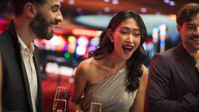 Attractive Multiethnic Female Taking Risks in a Casino and Celebrating a Winning Bet with Her Partner. Young Cheerful Asian Woman is Excited, Talking with Boyfriend and Clinking Champagne Glasses