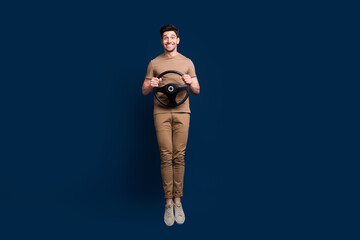 Canvas Print - Full size photo of good mood man dressed beige t-shirt jump hold steering wheel at driving lessons isolated on dark blue color background