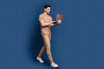 Poster - Full size photo of clever positive man dressed beige t-shirt typing email on laptop go empty space isolated on dark blue color background