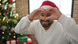© Krakenimages.com - African american man celebrating christmas doing heart shape with hands at home