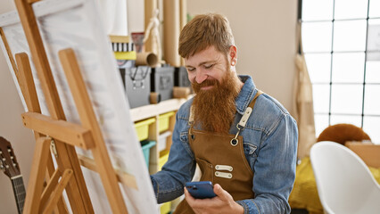 Canvas Print - Confident redhead young man, a smiling artist, carefully drawing on smartphone in art studio classroom