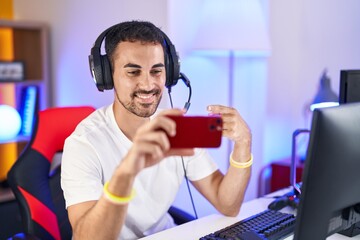 Wall Mural - Handsome hispanic man playing video games with smartphone smiling happy pointing with hand and finger