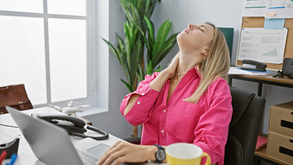 Sticker - A young, blonde woman in a pink shirt feeling neck pain at her office desk, exuding a mix of professionalism and discomfort.