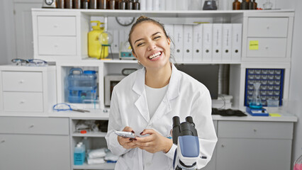 Canvas Print - Young beautiful hispanic woman scientist using smartphone smiling at laboratory