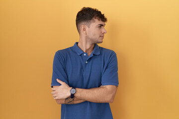 Canvas Print - Young hispanic man standing over yellow background looking to the side with arms crossed convinced and confident