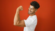 Handsome young hispanic man flexing muscles with a smile against a red wall background