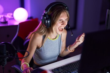 Canvas Print - Young blonde woman streamer playing video game with winner expression at gaming room