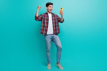 Sticker - Full length photo of good mood lucky man dressed plaid shirt rising fist winning game modern gadget isolated turquoise color background