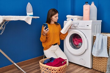 Poster - Young blonde woman using smartphone holding detergent bottle at laundry room