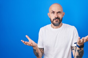 Poster - Hispanic man with tattoos standing over blue background clueless and confused with open arms, no idea concept.