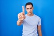 © Krakenimages.com - Young hispanic man standing over blue background pointing with finger up and angry expression, showing no gesture