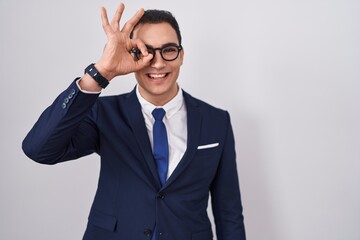 Sticker - Young hispanic man wearing suit and tie doing ok gesture with hand smiling, eye looking through fingers with happy face.