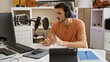 Hispanic man with headphones speaks into microphone in home studio setting, portraying a creative or podcasting scene.