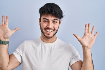 Sticker - Hispanic man with beard standing over white background showing and pointing up with fingers number ten while smiling confident and happy.