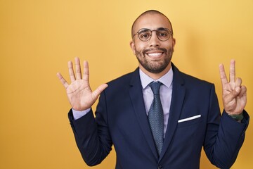 Poster - Hispanic man with beard wearing suit and tie showing and pointing up with fingers number seven while smiling confident and happy.