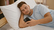 © Krakenimages.com - A young hispanic man with a beard lounging in a bedroom, looking at a smartphone while reclining on a pillow.