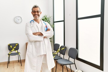 Wall Mural - Middle age grey-haired man doctor smiling confident standing with arms crossed gesture at clinic waiting room