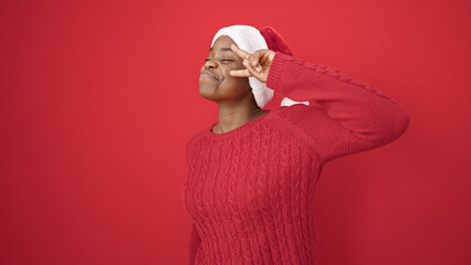 Poster - African american woman wearing christmas hat doing victory gesture over isolated red background