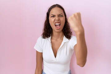 Wall Mural - Young hispanic woman wearing casual white t shirt angry and mad raising fist frustrated and furious while shouting with anger. rage and aggressive concept.