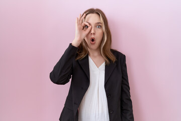 Poster - Young caucasian business woman wearing black jacket doing ok gesture shocked with surprised face, eye looking through fingers. unbelieving expression.