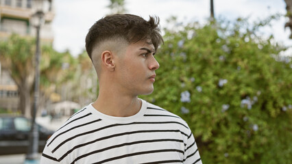 Poster - Handsome young hispanic man, expression of serious concentration, looking to the side in a sunny park, perfectly relaxed in cool, casual fashion â€“ a portrait of green outdoor, city lifestyle