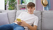 © Krakenimages.com - A smiling caucasian teenage boy relaxes on a sofa at home, casually using a smartphone.