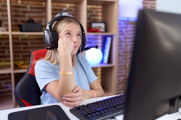 Canvas Print - Young caucasian woman playing video games wearing headphones with hand on chin thinking about question, pensive expression. smiling with thoughtful face. doubt concept.